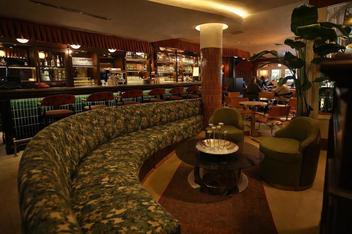 Kadıköy’deki BİAS Kitchen’ın sıcak atmosferinde, alevlerin dans ettiği uzun barın önünde kırmızı sandalyeler, tuğla duvar ve ışıklandırılmış bir ağaç; dışarıda gece manzarası görülüyor.